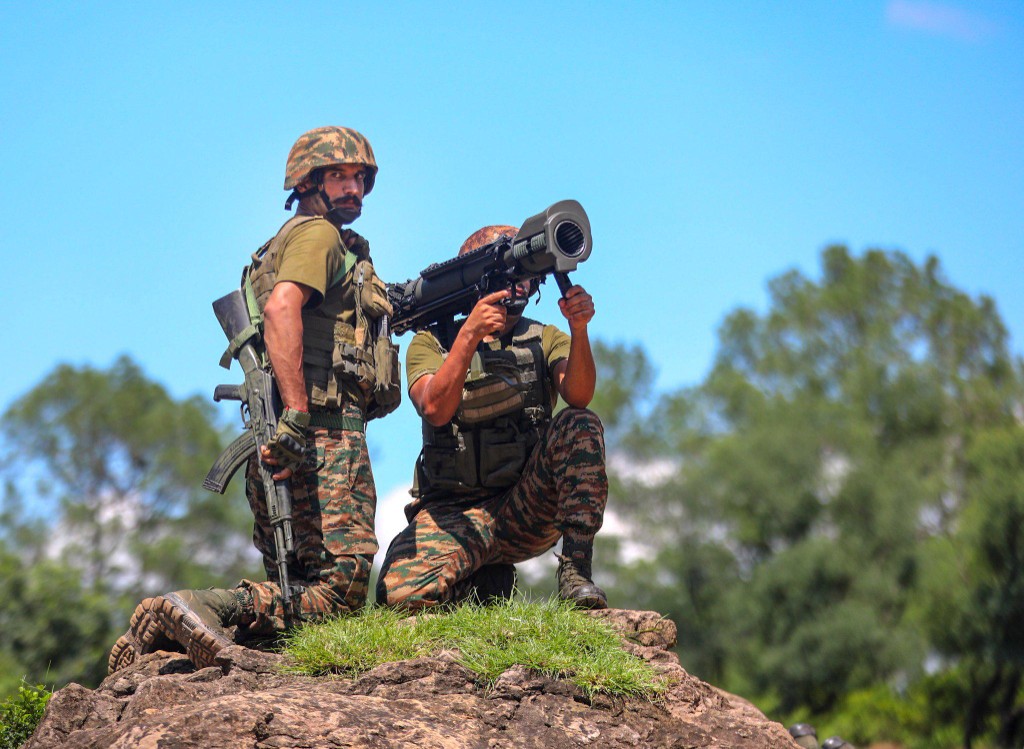 Two soldiers in combat dress hold position on a rock.