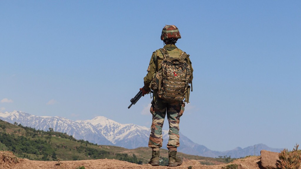 A soldier in combat dress looks out over snow-covered mountains.